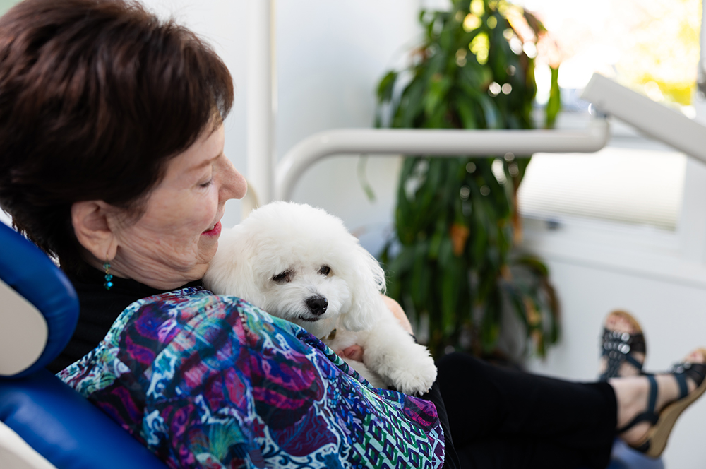 Patient holding an emotional support dog while relaxing in a dental chair at iCreate Smiles in Palo Alto